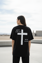 Frau trägt schwarzes Don't Give Up Oversized T-Shirt mit Backprint Kreuz He's Alive